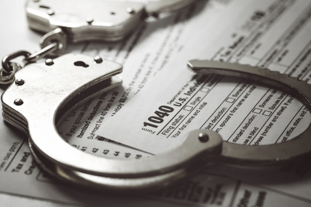 Handcuffs on top 1040 tax forms to represent tax evasion and tax fraud