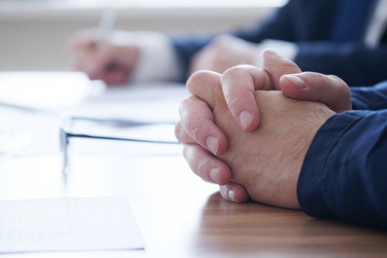 Folded male hands on a wooden table. Participant of negotiations, interviews, meetings. At the reception of a social worker, lawyer or employer. No face. Unrecognizable. Selective focus. Close-up